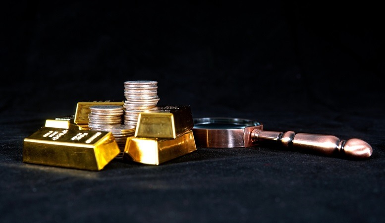 magnifying glass with gold bars and coins