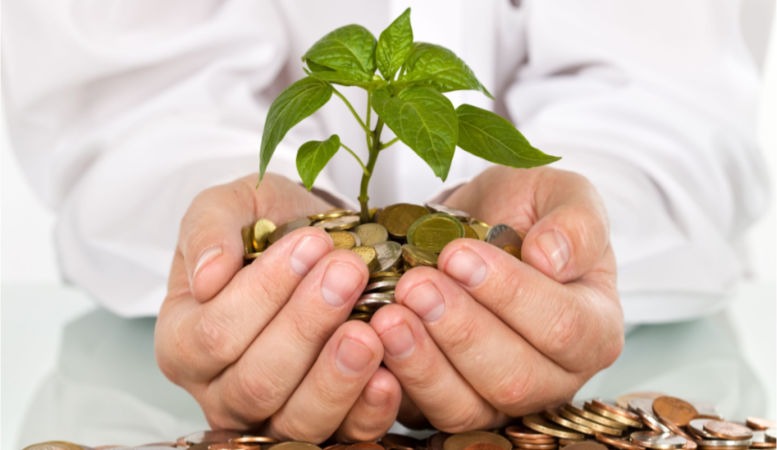 businessman holding plant sprouting from a handful of gold coins
