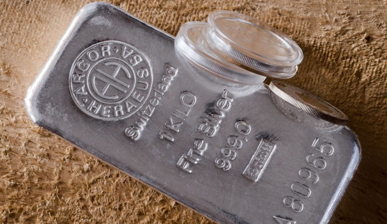 one kilogram fine silver bar and silver coins on rough wooden background