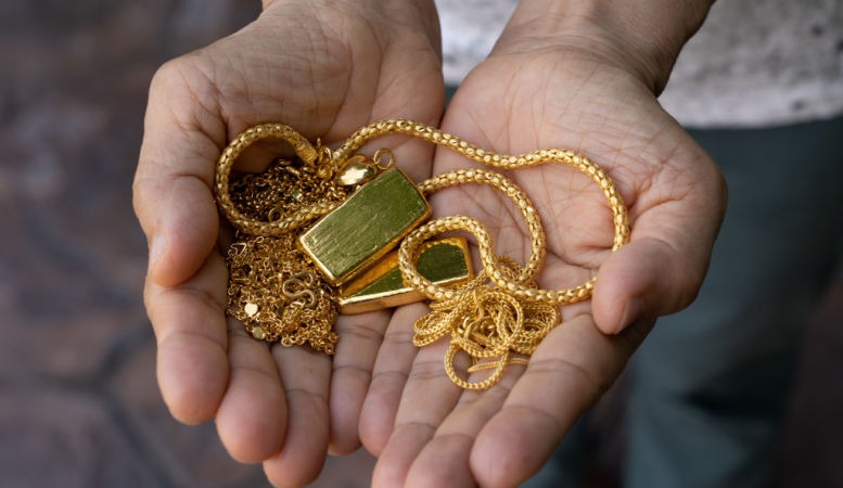 hand holding gold jewelries and gold bars
