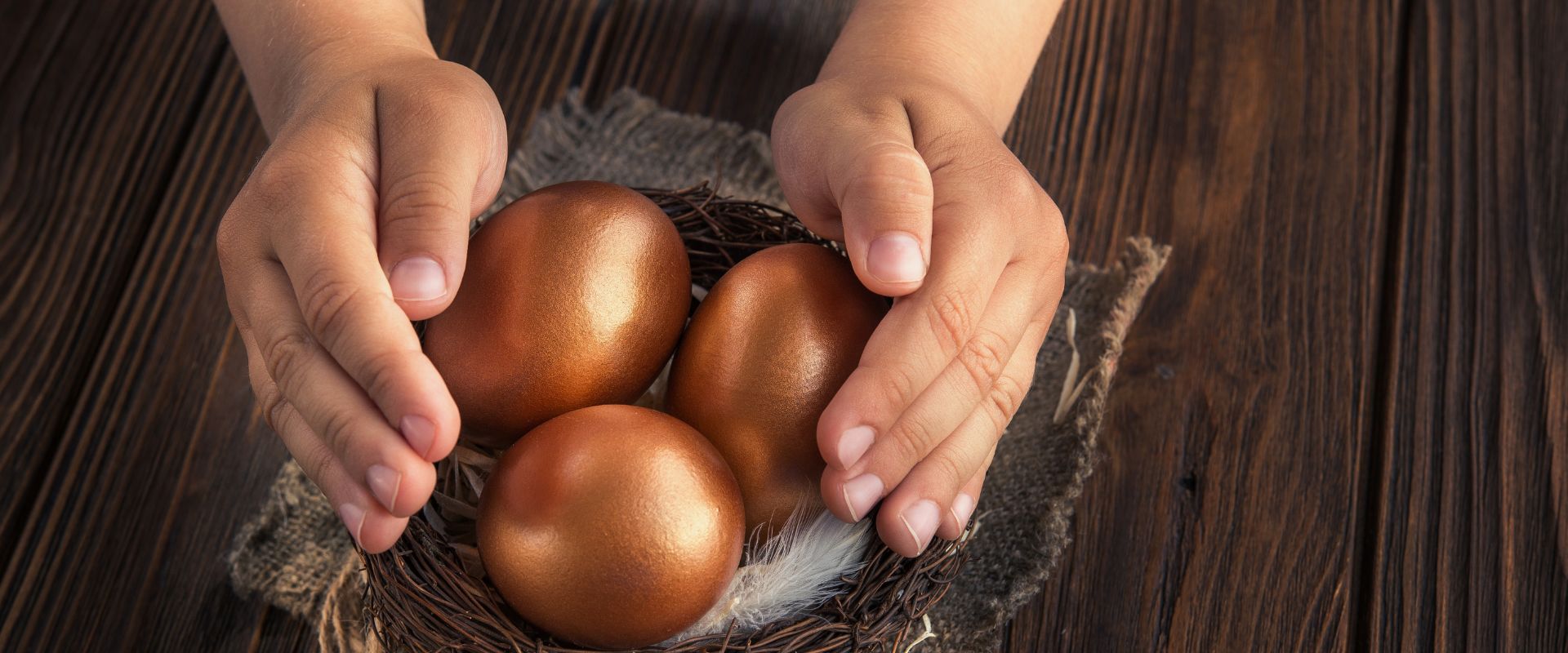 hand protecting three gold eggs in the nest